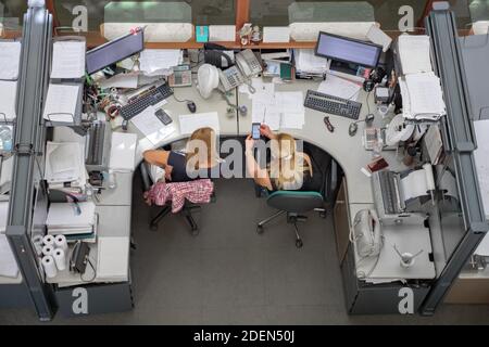 Top view. Workplace communication. Female demonstrate phone. Working days of office workers. Message on cell. Two woman, colleagues using smartphone Stock Photo