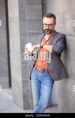 Handsome man in casual clothes checking for the time waiting for someone in the city, Man drinking take away coffee outdoor Stock Photo