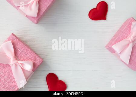 Boxes for small gifts in pastel colors and red satin hearts on a light background with a place for text. Advertising, poster. Stock Photo