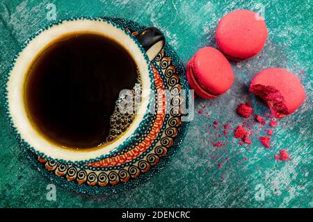 Pink strawberry macarons with an elegant colorful cup of freshly roasted coffee on an intense green grunge background. Nibble biscuits with crumbs. Stock Photo
