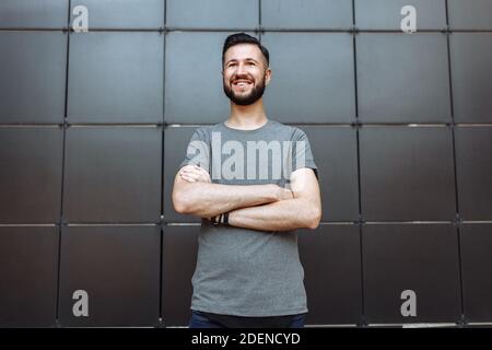 Portrait of a beautiful stylish guy, hipster dressed in a gray empty t-shirt standing on a black wall background. Stock Photo