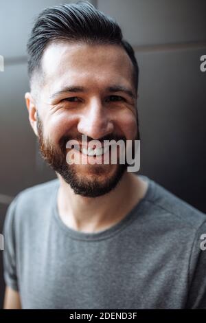 Portrait of a beautiful stylish guy, hipster dressed in a gray empty t-shirt standing on a black wall background. Stock Photo