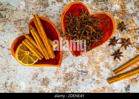 Cinnamon sticks, star anise and dried citrus in red bowls with a heart shape on a light grunge background. Winter spices used with mulled wine. Stock Photo
