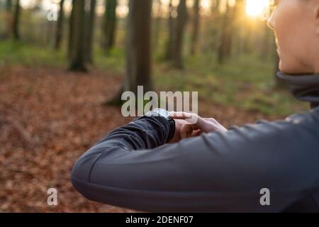 Woman checking her smartwatch while running through the woods Stock Photo