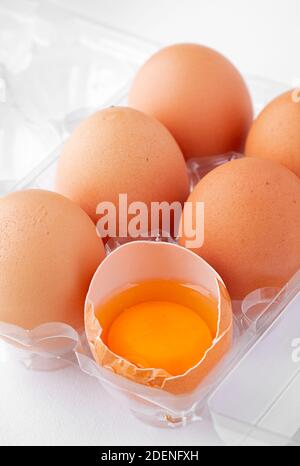 Half dozen of extra large free range eggs with one cracked exposing the rich yellow yolk Stock Photo