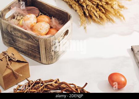 A simple rural composition. Painted in pastel warm colors Easter eggs in a wooden box in sunlight on a white table near the window Stock Photo