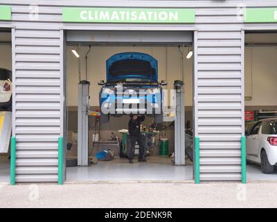 Service bay scene. Blue car with bonnet open raised on an inspection ramp. Employee looking up at underside of the vehicle. clean tiled floor , tools Stock Photo