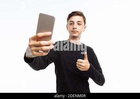 Portrait of an emotional teenager who takes a selfie on a smartphone, in a black t-shirt, on a white background, Stock Photo