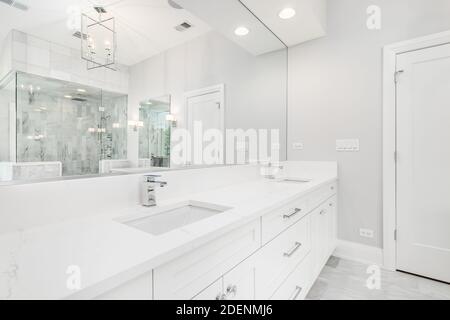 A large luxurious bathroom with a stand alone tub, white vanity, and a glass stand up shower with marble tiles and bench seat. Stock Photo