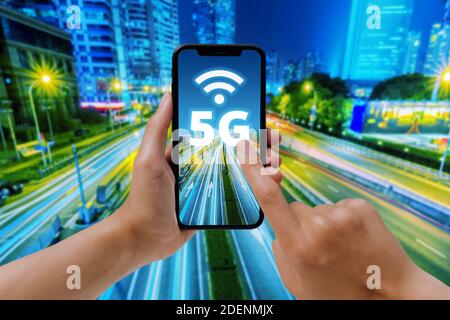 Fast 5g network concept. A woman tapping on a smartphone screen with a city landscape in the background. 5G and wifi symbol. Stock Photo
