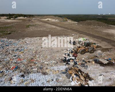 Top drone view of dump with different types of garbage. Tractor carries waste on landfill of big city. Stock Photo