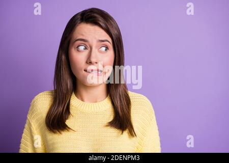 Photo portrait of guilty troubled brunette girl biting lip looking at blank space wearing knitted sweater isolated on vivid color violet background Stock Photo