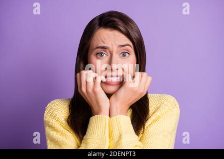 Photo portrait of nervous troubled brunette girl biting fingers on both hands worrying wearing yello sweater isolated on vivid color violet background Stock Photo