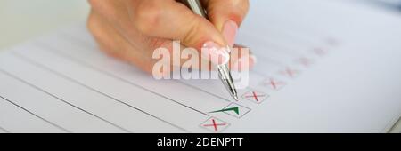 Woman's holding pen on table lies a document with red and green check marks Stock Photo