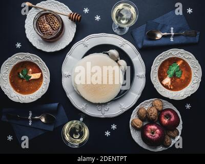 Table with Christmas dinner for two. Plates of fish soup, wafers, honey, garlic bulbs, apples, walnuts, glasses of wine and decoration. Overhead view. Stock Photo