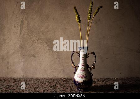 Autumnal still life of ears of wheat in a ceramic jar. Dark and gloomy mood with brown and golden tones. Melancholy and nostalgia concept Stock Photo