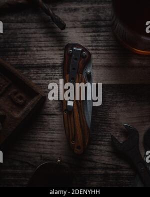 Folded knife displayed on a wooden table surrounded by various work tools Stock Photo