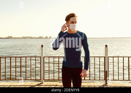 Handsome caucasian male in sportswear poses on the beach wearing a mask.