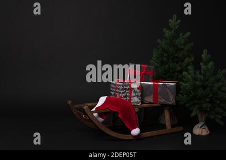 Rustic sleigh with gift boxes and Santas hat next to Christmas trees Stock Photo