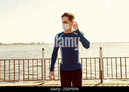 Handsome caucasian male in sportswear poses on the beach wearing a mask.