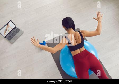 Woman watching online workout lesson and doing back extension exercise on fit ball Stock Photo