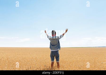 the man raised his hands to the sky, against the background of a wheat field, the guy in the cap and shirt Stock Photo