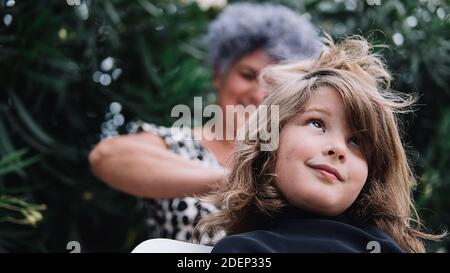 young girl getting his haircut by a happy woman in the garden. She is happy and looking up. Stock Photo