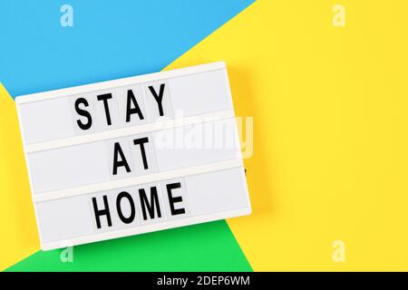 Lightbox with text STAY AT HOME on yellow, green and light blue background. Top view Stock Photo