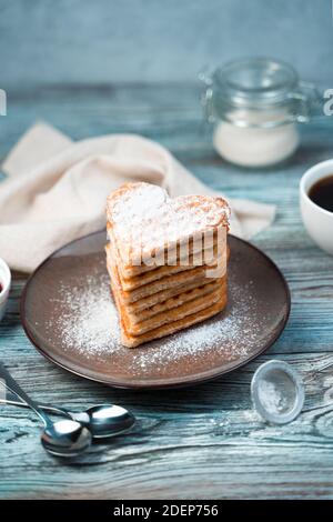 Heart of waffles sprinkled with powdered sugar in a brown plate on a wooden gray-blue background. Stock Photo
