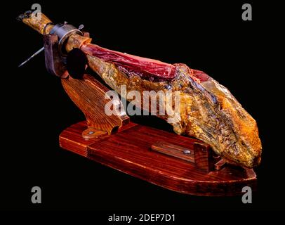 closeup of a whole piece of spanish serrano ham in a stand on a black background Stock Photo