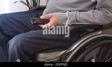 Man on wheelchair looking TV and using remote control in living room. Stock Photo