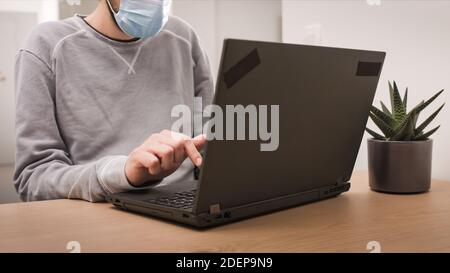 Man remotely working from home using laptop with face mask, looking at screen with virtual web chat. Stock Photo
