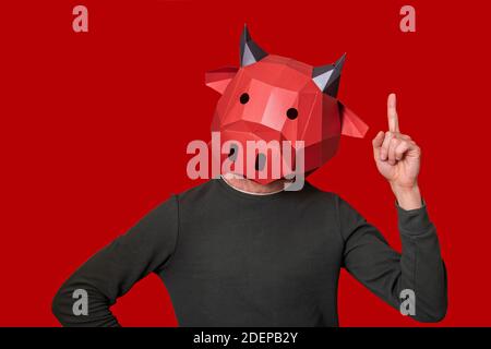 Young man in red 3d mask of bull cow on the head isolated background. The person gestures to show that he has an idea. Blank for banner, template, pla Stock Photo