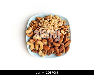 Small plate of assorted nuts with walnuts, cashew, almonds and pine nuts, on a light blue coffee coaster on white background Stock Photo