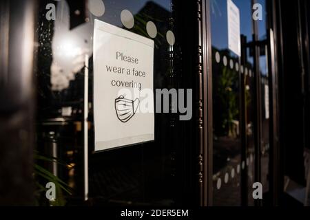 Coronavirus Covid-19 information sign saying please wear a face mask covering in a shop window while shops were shut during lockdown in London on an empty shopping high street in England, Europe Stock Photo