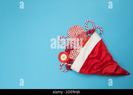 Heap of sweets in a Santa Claus hat. Christmas red candy canes and lollipops on blue background. Merry Christmas sweets and Happy New Year concept Stock Photo