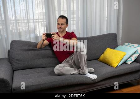 Mature man (44 years old) sitting on the couch and watching movie on his smartphone. Stock Photo