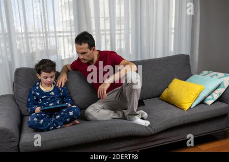 Mature man (44 years old) sitting next to his son (6 years old) with his hand on his shoulder. Stock Photo