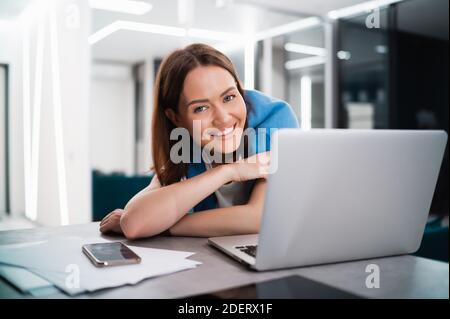 Smiling woman sitting in the kitchen and using the laptop. Working from home in quarantine lockdown. Social distancing Self Isolation. Stock Photo