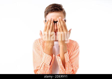 Young man closed his eyes with both hands, concept: fear in his eyes, guy in the Studio on a white background, in a shirt in a cage Stock Photo