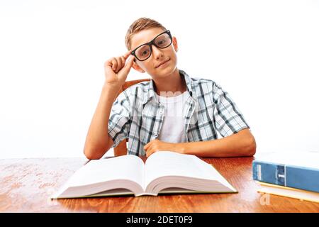 Young handsome teen guy reading book sitting at table, schoolboy or student doing homework, in Studio on white background Stock Photo
