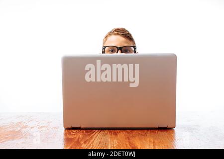 The face of a young man looks out from under the laptop, a teenager hiding behind a laptop in the Studio Stock Photo
