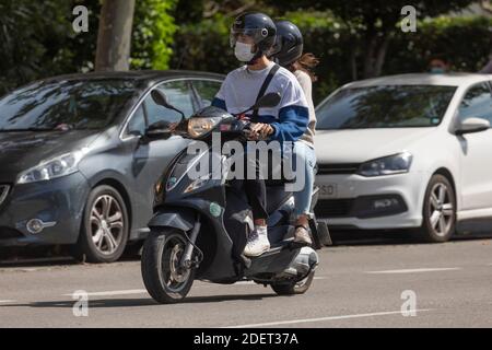 Madrid, Spain - Sep 26, 2020: A young boy and girl, wearing a helmet and a protective face mask, ride together on a motorcycle, scooter type, in the R Stock Photo