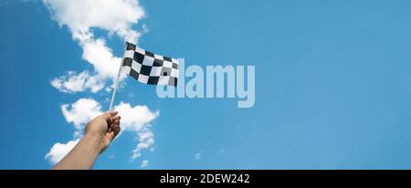 checkered race flag in hand over blue sky Stock Photo