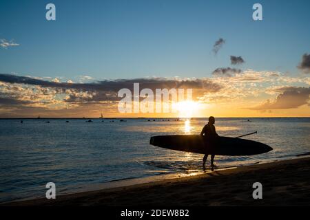 Stand up Paddler walks out of hawaii ocean at sunset Stock Photo