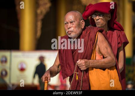 Senior Buddhist monk dressed in red robe walking on grounds of Shwedagon Pagoda complex, Yangon, Myanmar Stock Photo