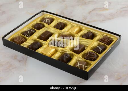 Open box of assorted Belgian chocolates in gold colored foil on table Stock Photo