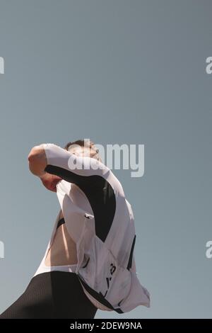 Cyclist unzips jersey during summer from below perspective Stock Photo