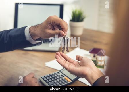 Real estate broker agent giving house keys to client after finish making rental agreement in the office Stock Photo