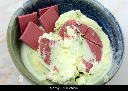 Layered pistachio sweet cream and ruby chocolate ice cream with ruby chocolate candy pieces on side in ceramic bowl on table Stock Photo